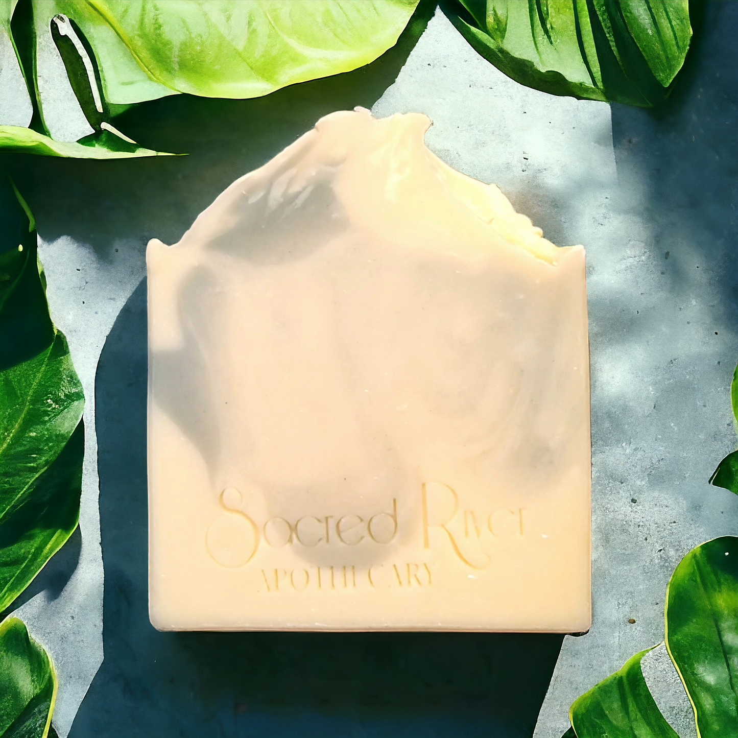 Delicate indigo blue swirl and light cream soap bar with Persian salt sprinkled on teaxtured soap top. Monstera leaves nestle around soap sitting on a cool grey concrete slab